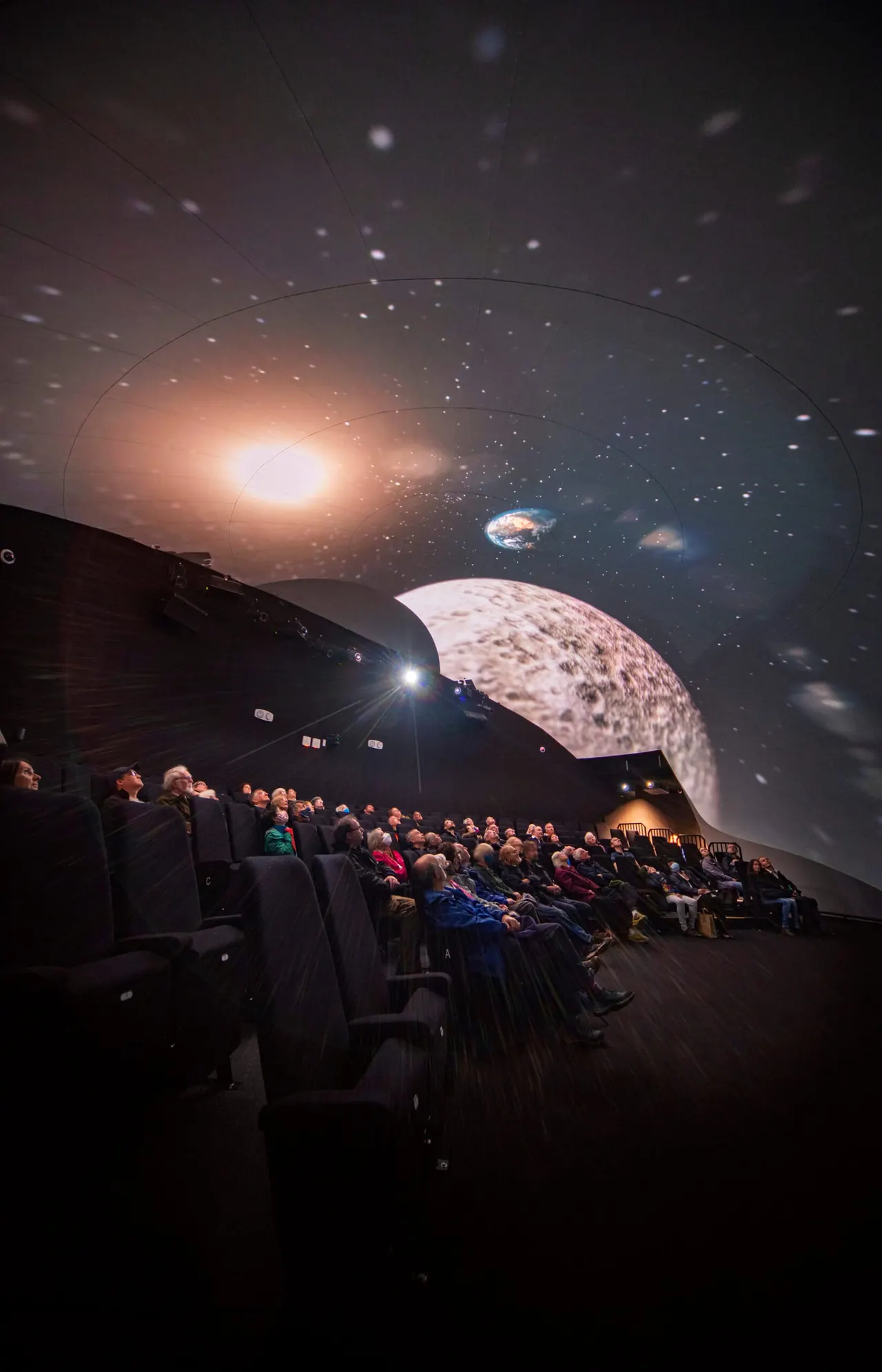 Planetarium audience watching an immersive sky show projection of planets and stars on a domed ceiling.