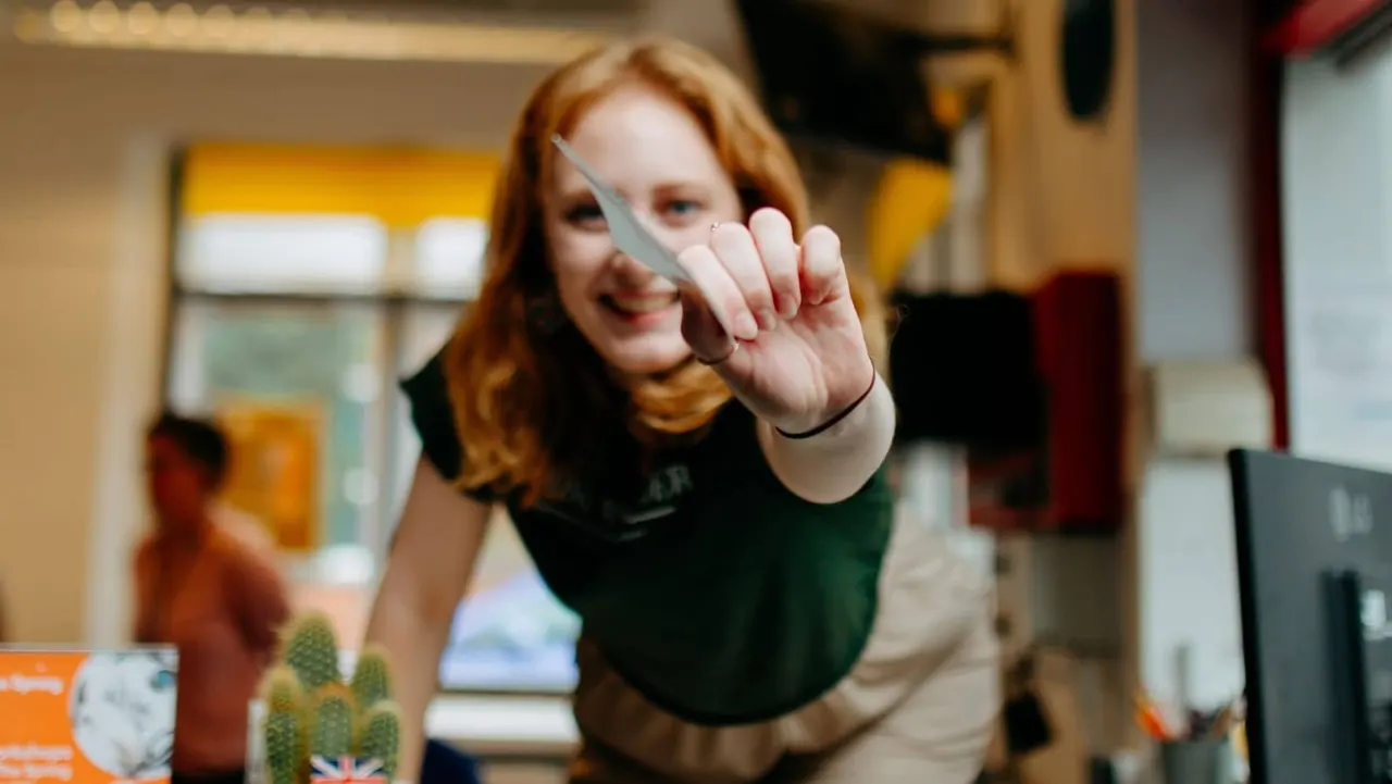 Child holding a small cactus plant and smiling at camera indoors.