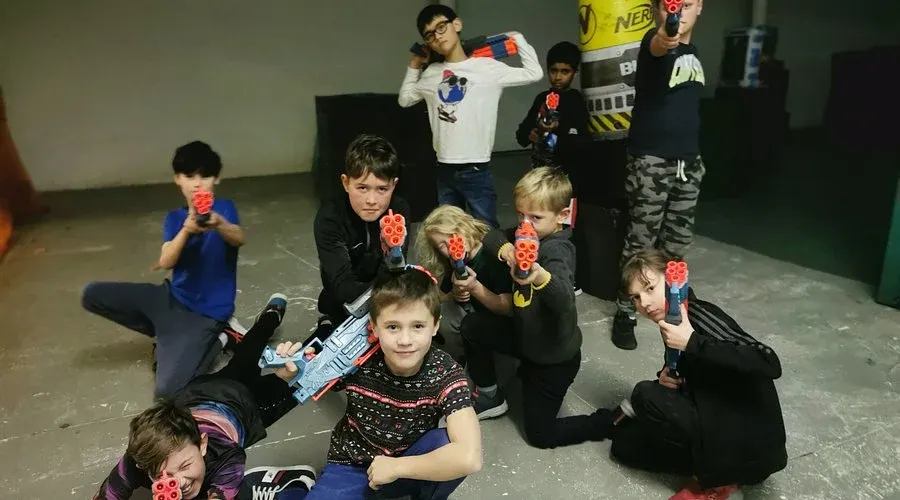 Group of children holding toy foam dart blasters, posing together indoors at an activity centre.