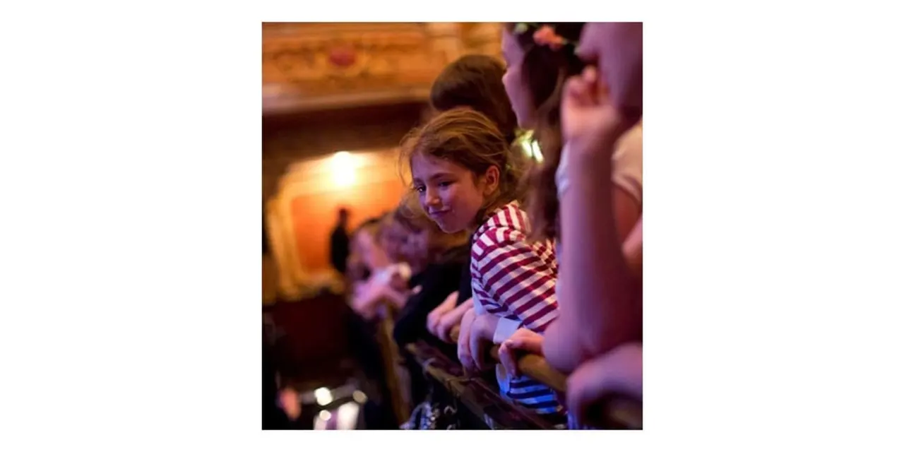 Young child in striped shirt smiling whilst enjoying an indoor activity with other visitors.