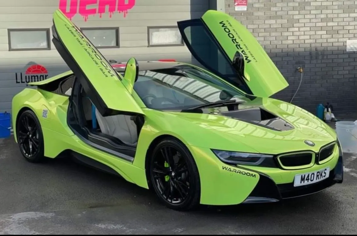 Bright lime-green sports car with open gull-wing doors parked outside a brick building.
