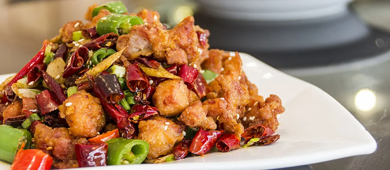 Crispy fried meat cubes topped with dried chillies, spring onions and sesame seeds on a white plate.