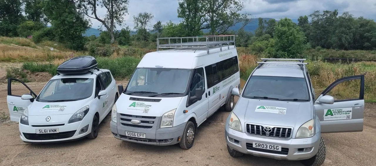 Three white adventure activity vehicles parked on a dirt ground with trees and mountains in the background.