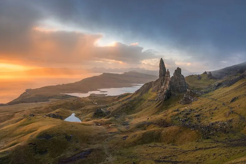 A dramatic highland landscape with distinctive rocky peaks, lochs and moorland beneath a golden sunset sky.
