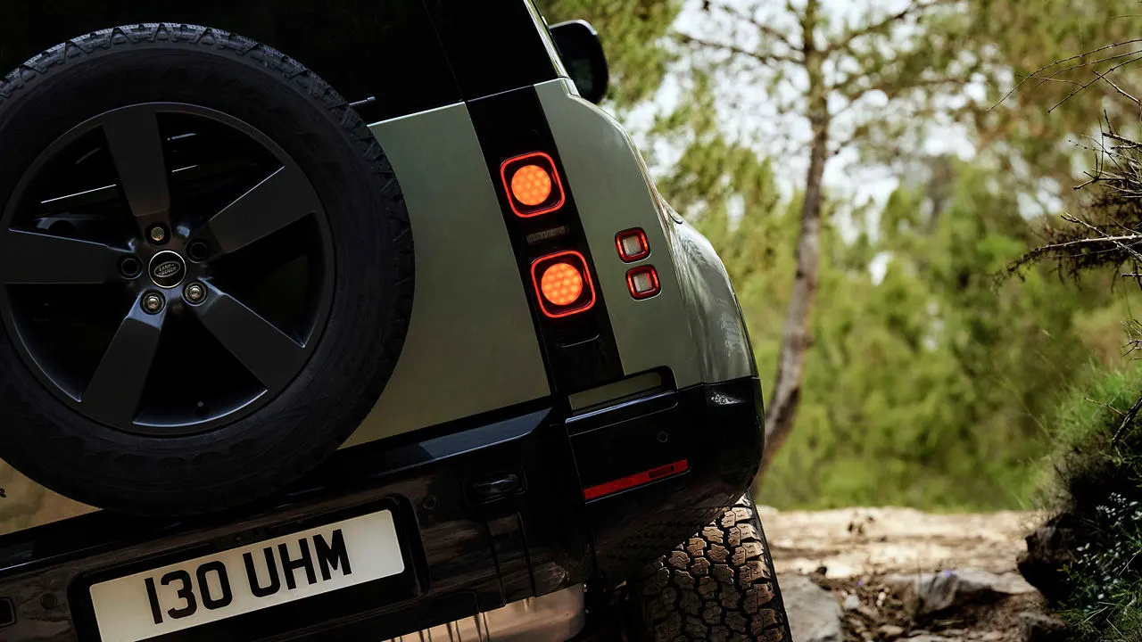 Close-up of the rear of a modern Land Rover vehicle with illuminated tail lights, parked outdoors with trees visible in the background.