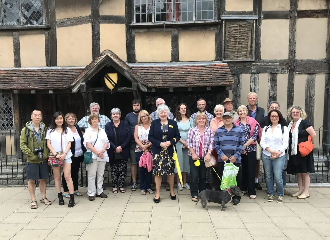 Group of tourists and guides posing together outside a historic timber-framed building with a small dog.