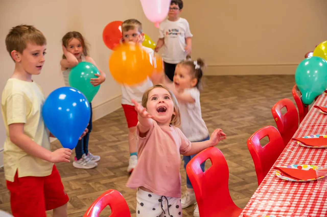 Young children playing with colourful balloons at an indoor birthday party celebration.