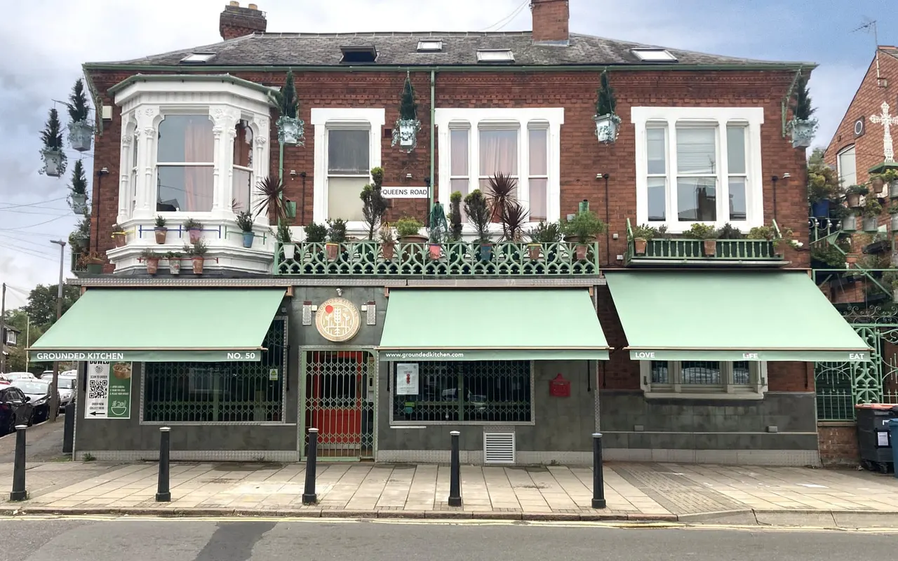 Exterior of a brick restaurant building with green awnings and large windows on Queens Road.
