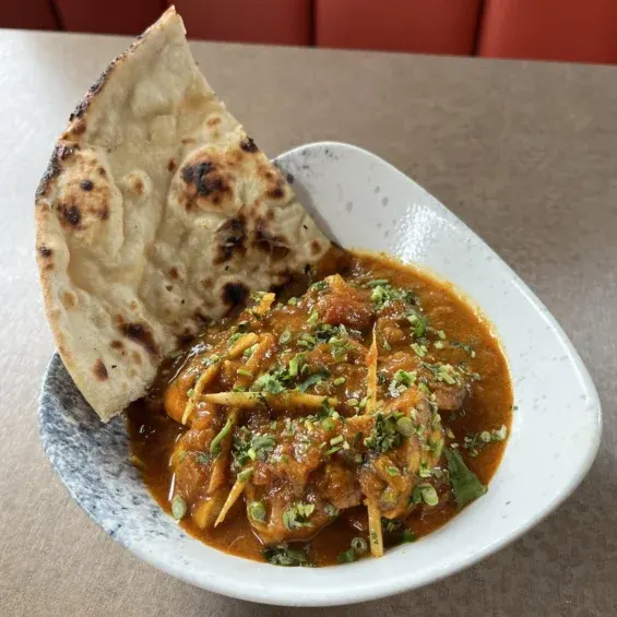 Naan bread served with a spiced curry dish garnished with fresh herbs on a white plate.