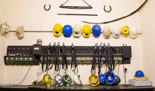 Safety helmets and tools organized on a wall-mounted rack in a mining facility.
