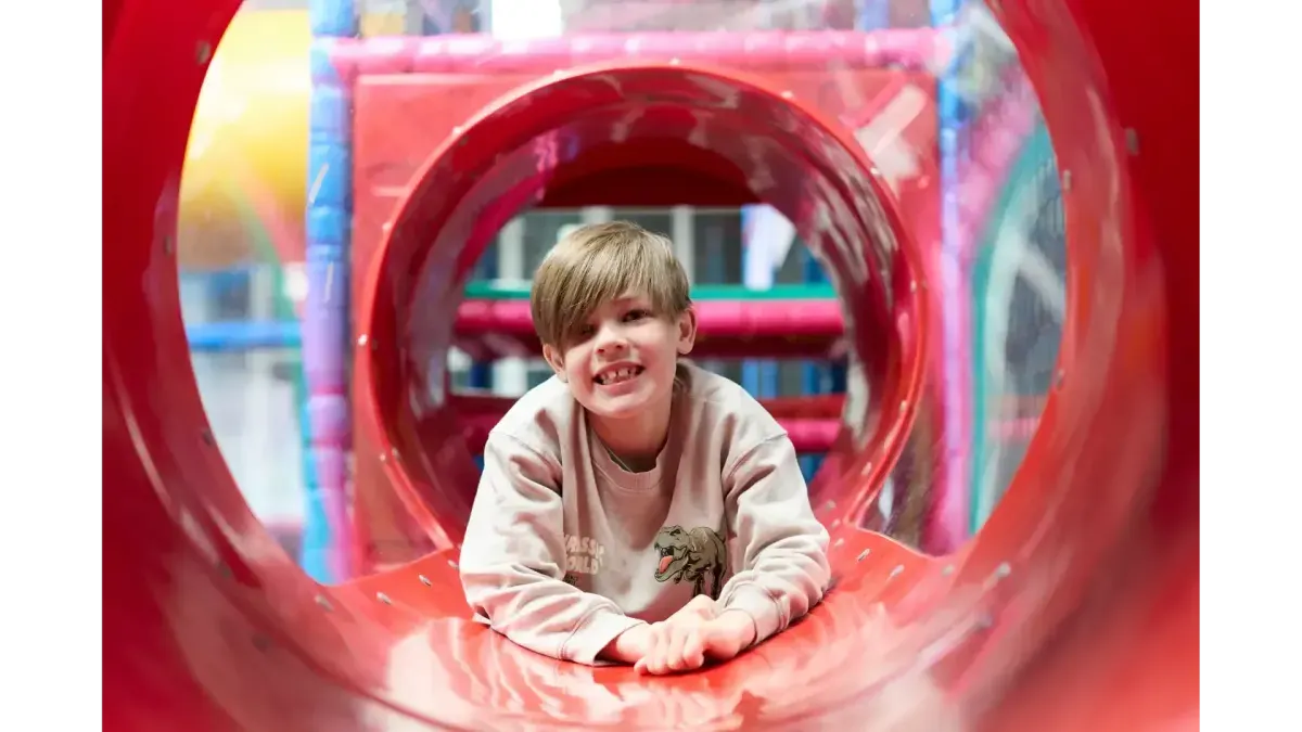 Child crawling through a red inflatable tunnel at an indoor play facility.