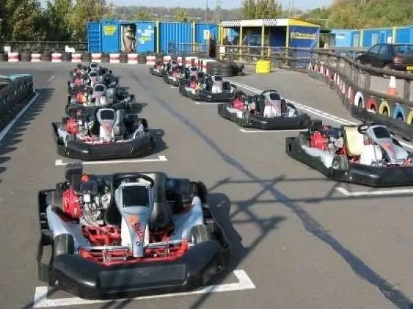 Multiple go-karts with drivers lined up on an outdoor track circuit at a leisure venue.