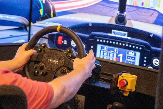 Person's hands on racing steering wheel inside a virtual reality racing simulator cockpit.