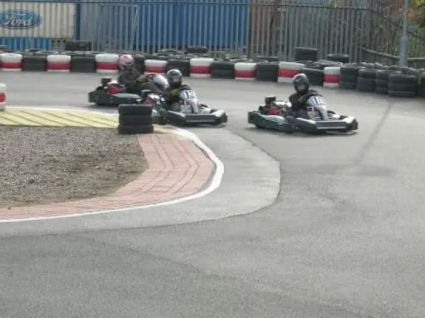 Two people in helmets drive go-karts around a track bordered by red and black tyres.