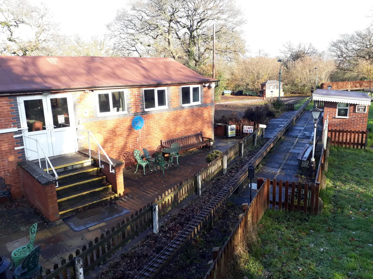 Miniature railway station buildings with narrow-gauge track in the foreground, brick pavilion and seating area, bare winter trees in background.