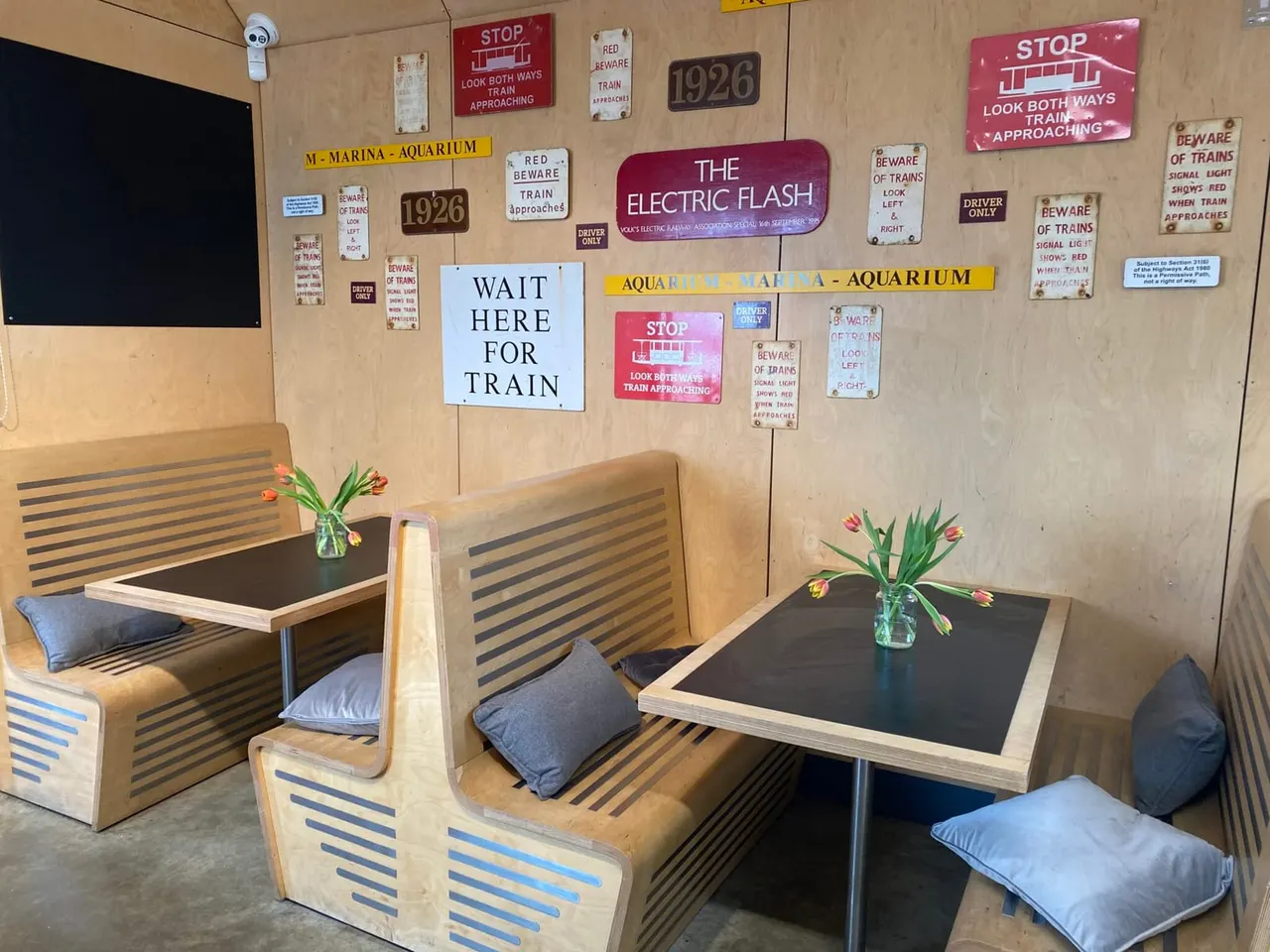 Interior seating area with wooden booths, black tables, and vintage railway-themed signage decorating the walls.