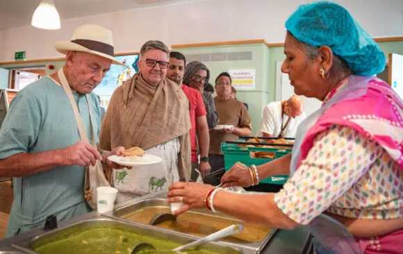 Visitors queue to receive food served by staff at a temple dining hall.