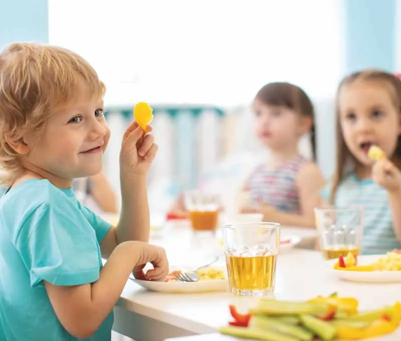 Young children eating a healthy meal together at a table indoors.