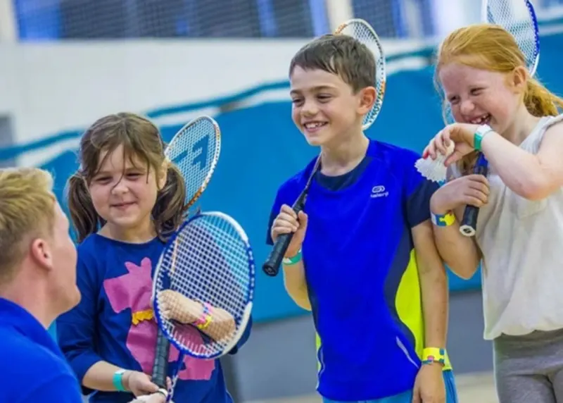 Group of children holding tennis rackets and smiling during an indoor tennis lesson.
