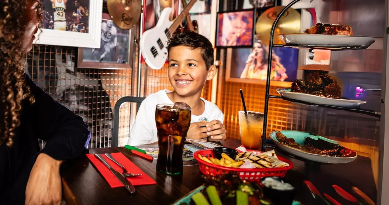 Child smiling at table with soft drink and food baskets in a themed restaurant interior.