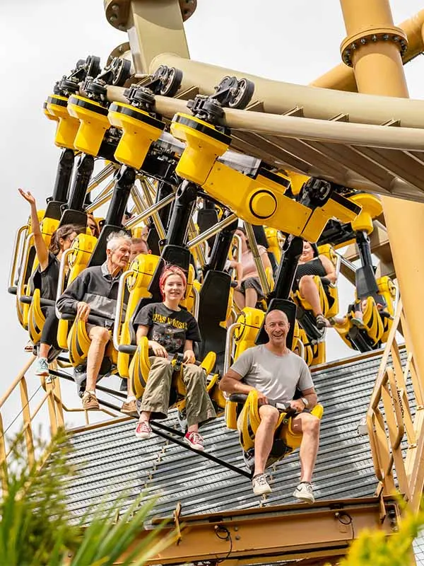 Visitors experience a roller coaster ride with yellow and black cars on the Flight of the Pterosaur attraction.