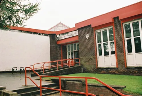 Modern brick building with red roof and trim, featuring a lawn and red metal ramp entrance.