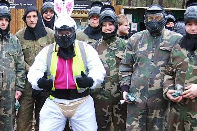 Group of people wearing camouflage uniforms and protective masks at a paintball venue.