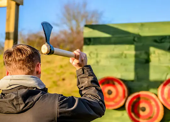Person holding an axe about to throw at a target during an axe-throwing activity, with bullseye targets visible in the background.