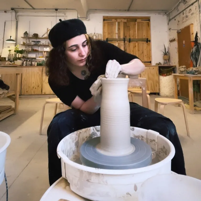 Woman shaping clay on a pottery wheel in a studio workshop.