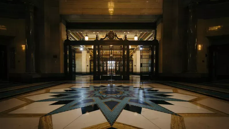 Grand lobby interior with geometric floor pattern and ornate black doors, lit by warm lighting.