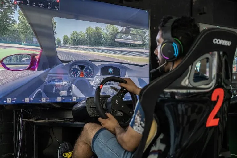 Person holding a racing wheel controller whilst playing a racing simulator game on a large screen display.