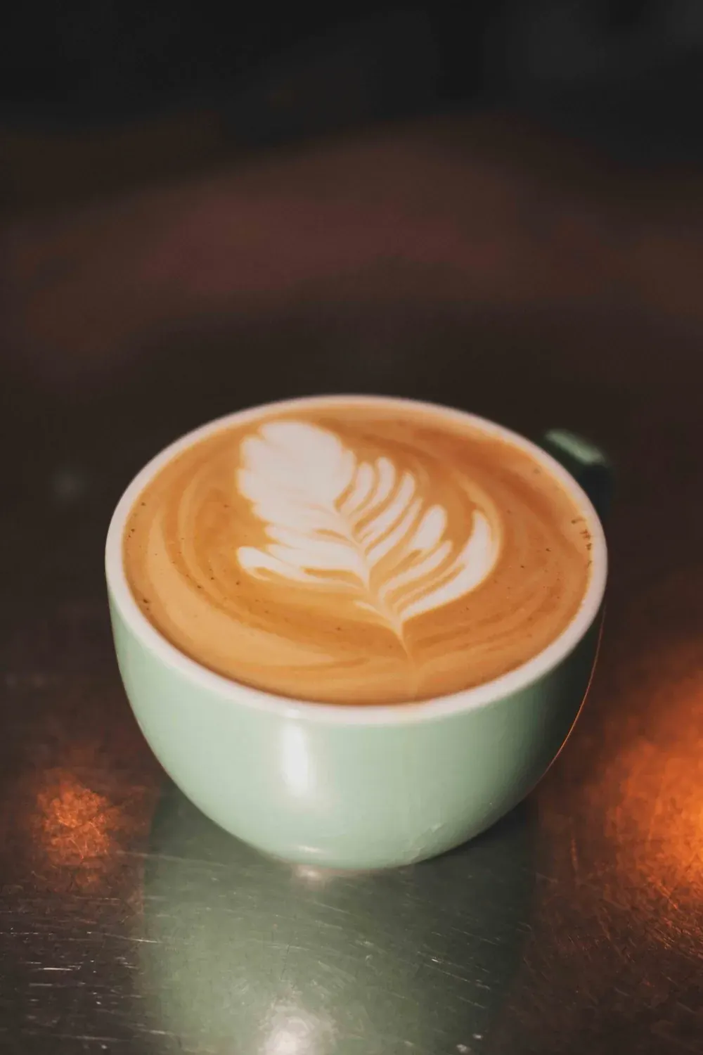 Latte with latte art in a pale green cup on a dark surface.