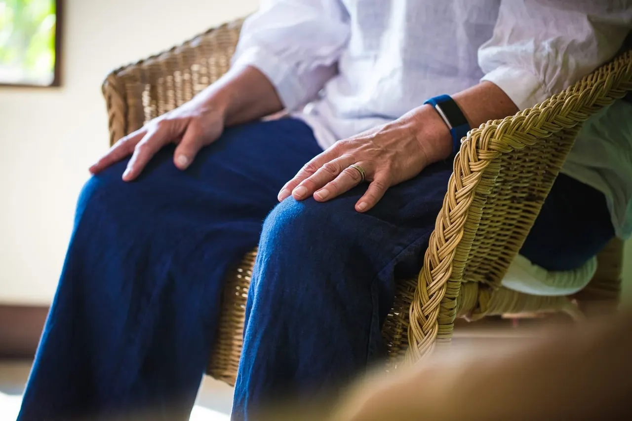 Two people sit together on wicker chairs, hands resting on their laps in a calm, supportive moment.