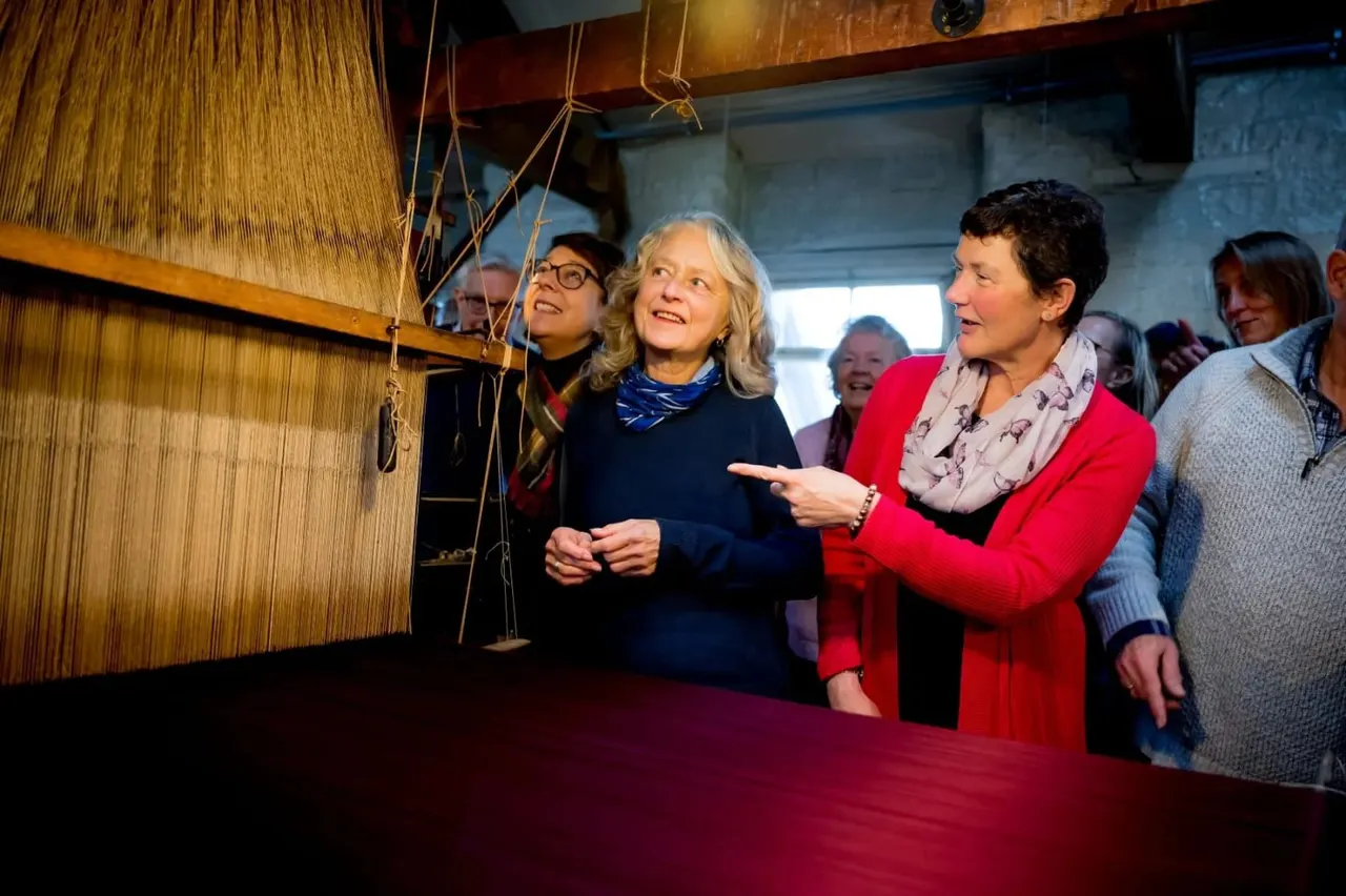 A group of visitors examine a large wooden loom during a guided tour at a museum.