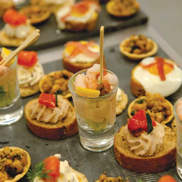 Assorted canapés and appetisers arranged on a slate surface, including toasted bread bases with toppings and small glasses with drinks and garnishes.