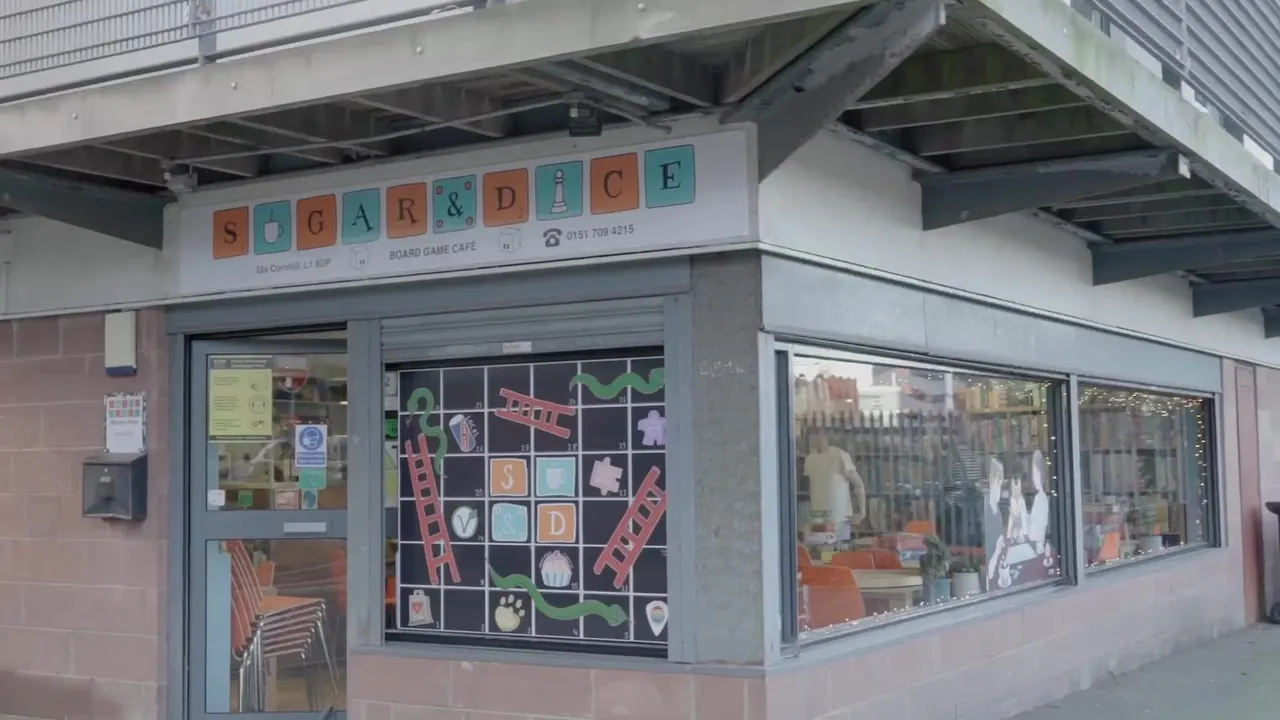 Exterior storefront of a board game café with colourful signage and display windows showing the interior seating and gaming area.