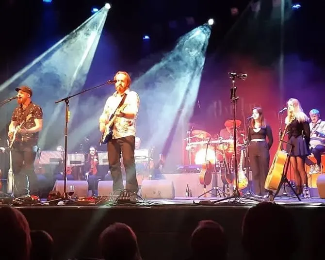 Band performing on stage with dramatic lighting and multiple musicians playing guitars and other instruments.