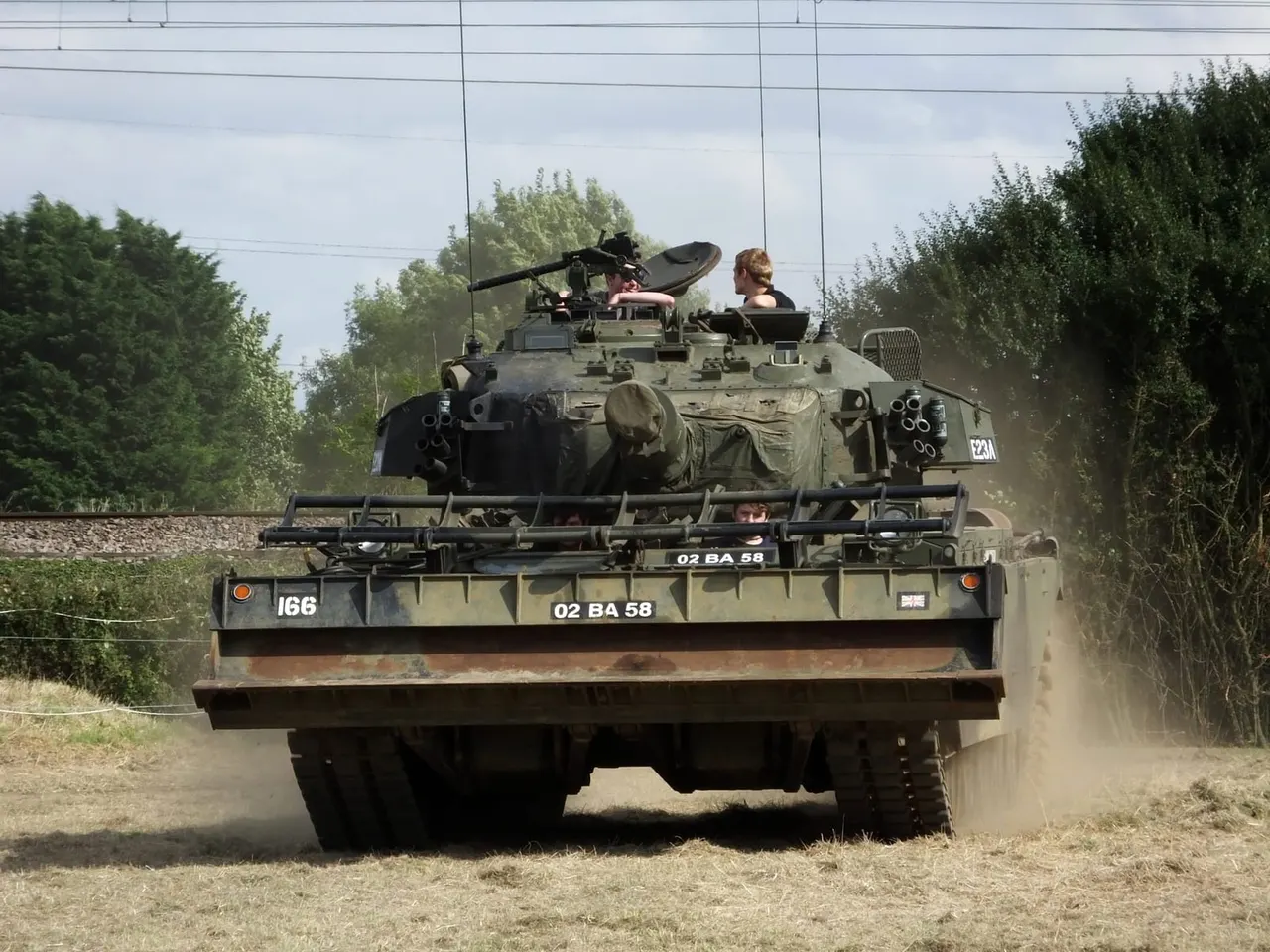 Two people operating a military tank with mounted weapons during an outdoor driving experience.