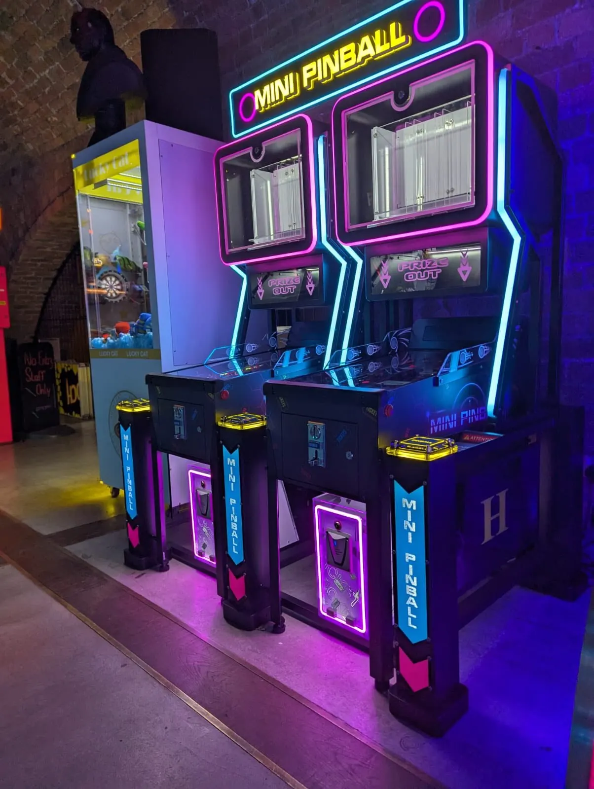 Neon-lit mini pinball arcade machines with magenta and cyan trim in an indoor games venue.