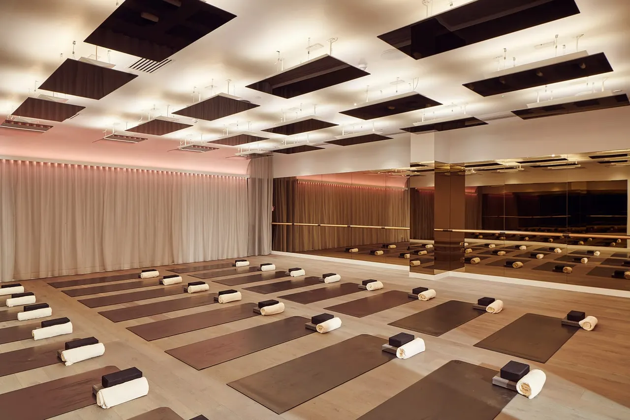 Modern yoga studio with multiple mats arranged in rows, rolled towels at the head of each mat, and mirrored walls reflecting the space.