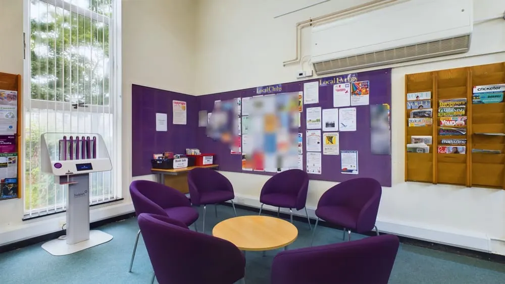 Purple chairs arranged in a circle around a wooden table in a modern library meeting space with purple display boards.