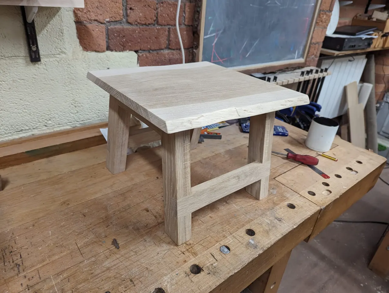 Unfinished wooden side table with rectangular top and open shelf base in a workshop setting.