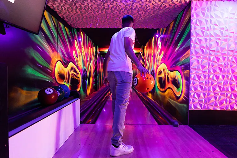 Person bowling in a brightly lit lane with neon graphics and purple lighting.