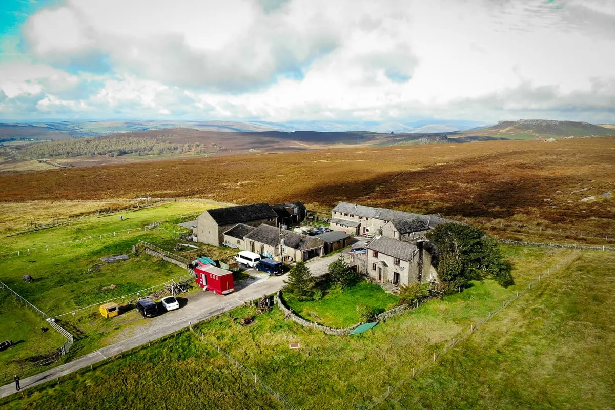 Aerial view of a stone farmhouse and outbuildings in rolling Scottish moorland with mountains in the distance.