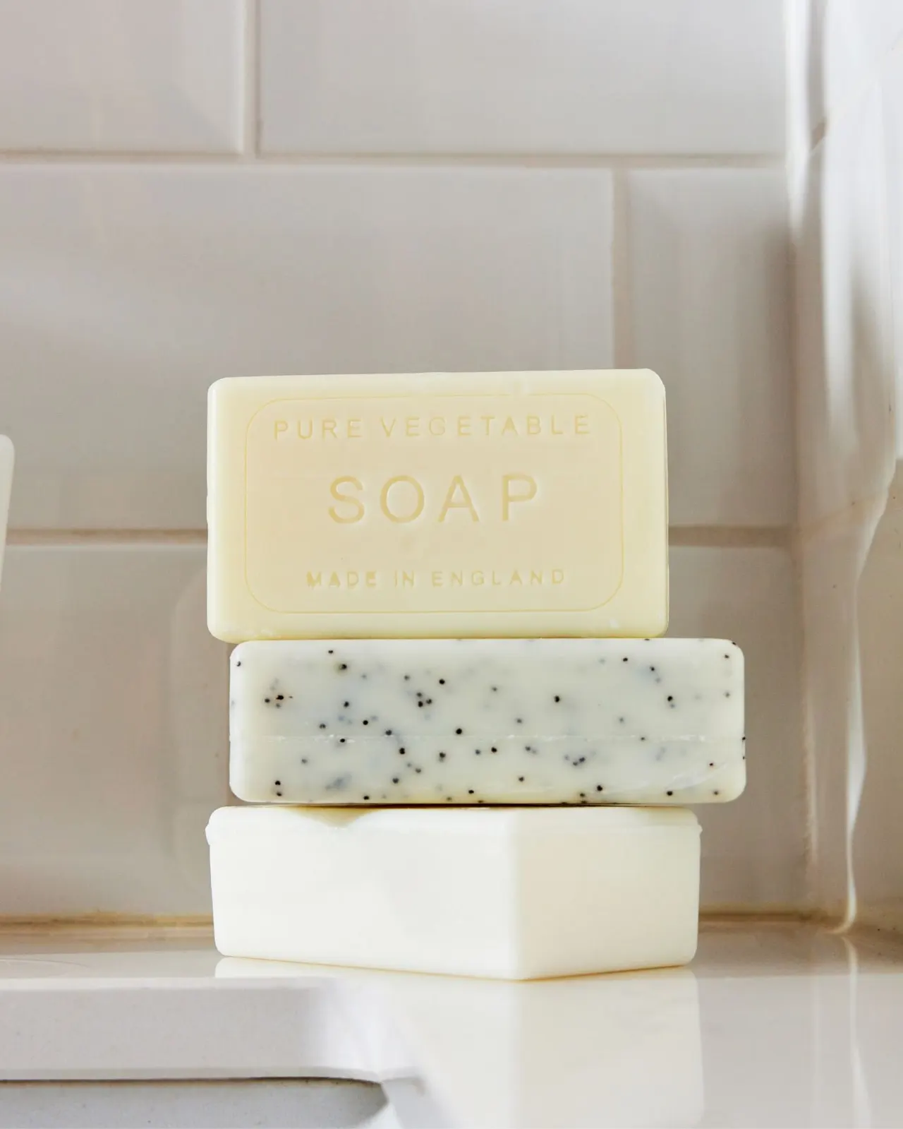 Three bars of pure vegetable soap stacked against a tiled wall.