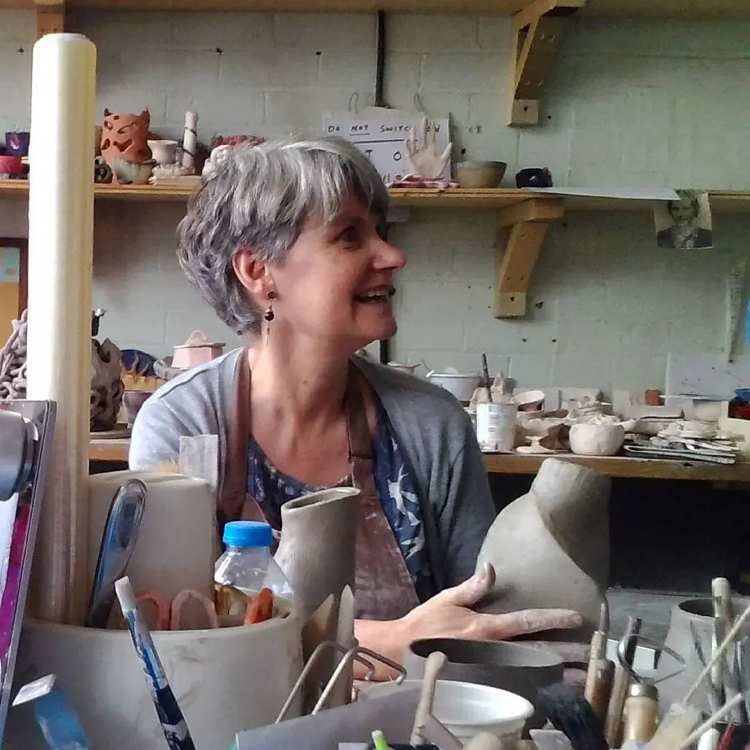 Woman in pottery studio working with clay, surrounded by ceramic tools and unfired pottery pieces.
