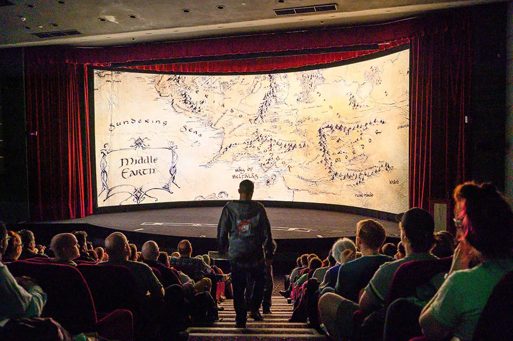An audience watches a large cinema screen displaying a fantasy map labelled "Middle Earth" during a film screening.