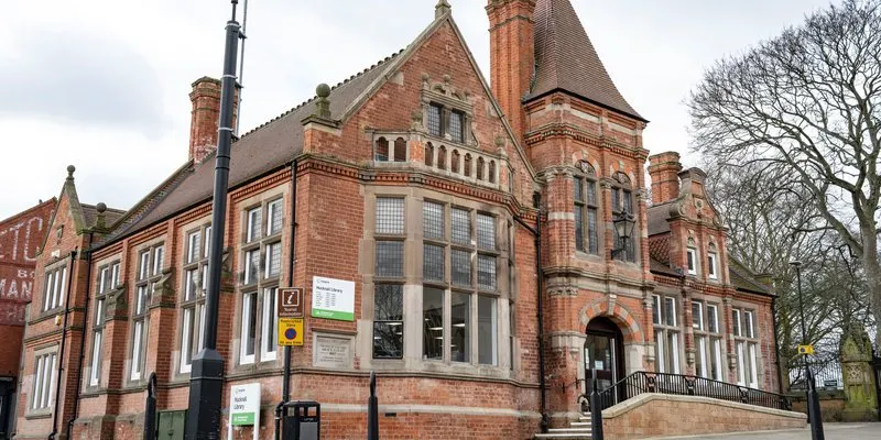 Victorian red-brick building with turrets and ornate architectural details, bare winter trees visible beside it.