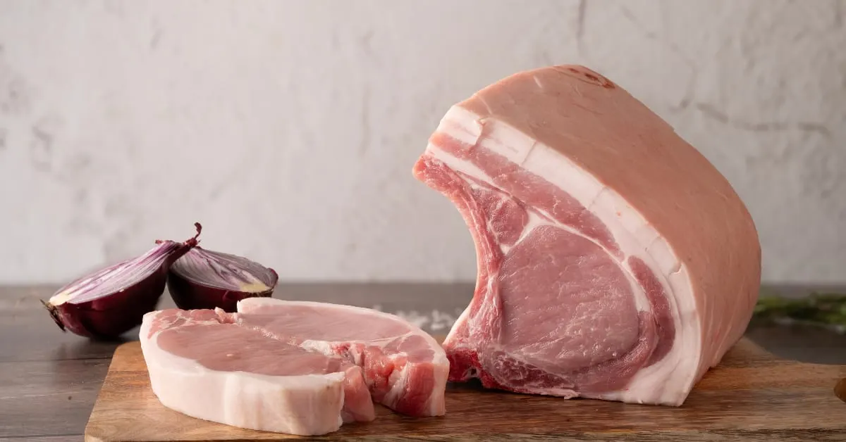Raw pork chops and a joint displayed on a wooden board with red onion.
