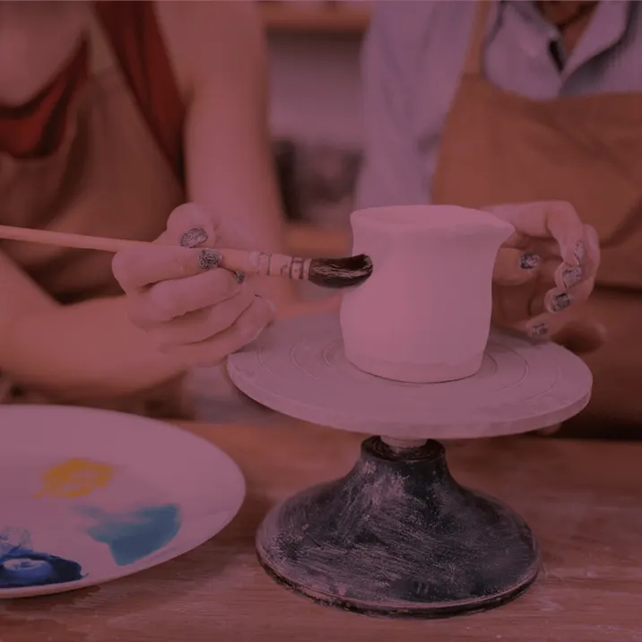 Child painting a ceramic mug on a pottery wheel at a pottery painting studio.
